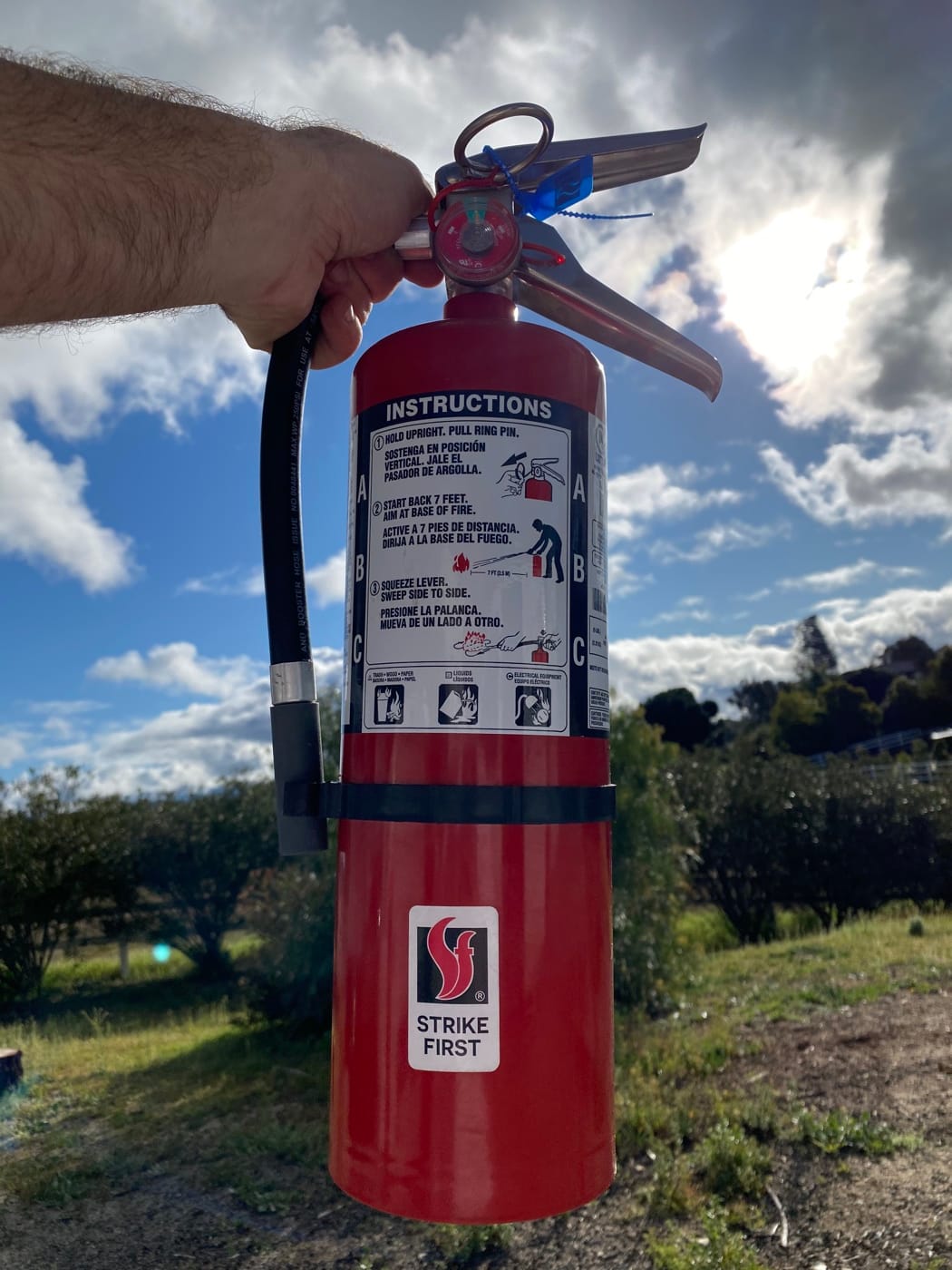 A hand holding a red portable extinguisher outdoors beneath a blue sky