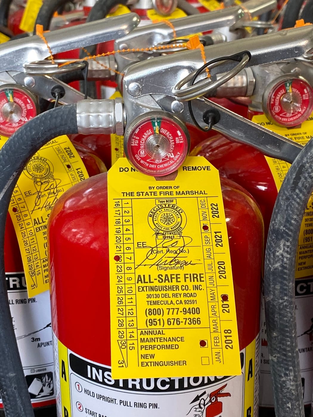 Close-up of an extinguisher handle, gauge, and yellow All-Safe service tag