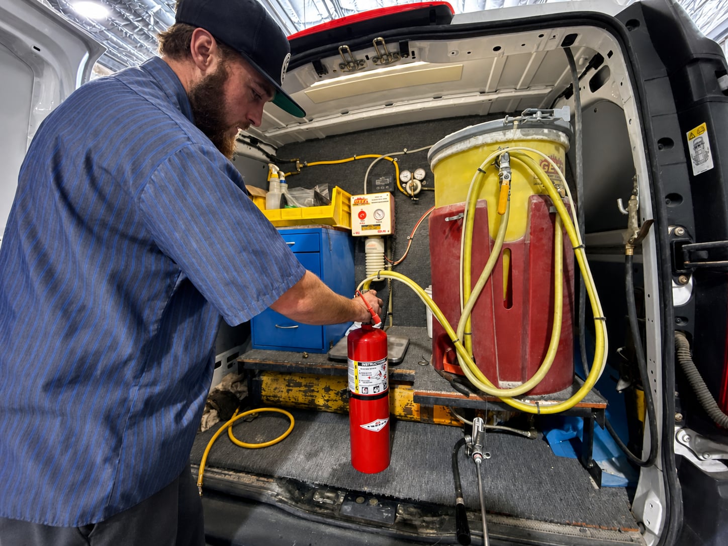 AI-enhanced company photo of a bearded technician recharging an extinguisher at the service van