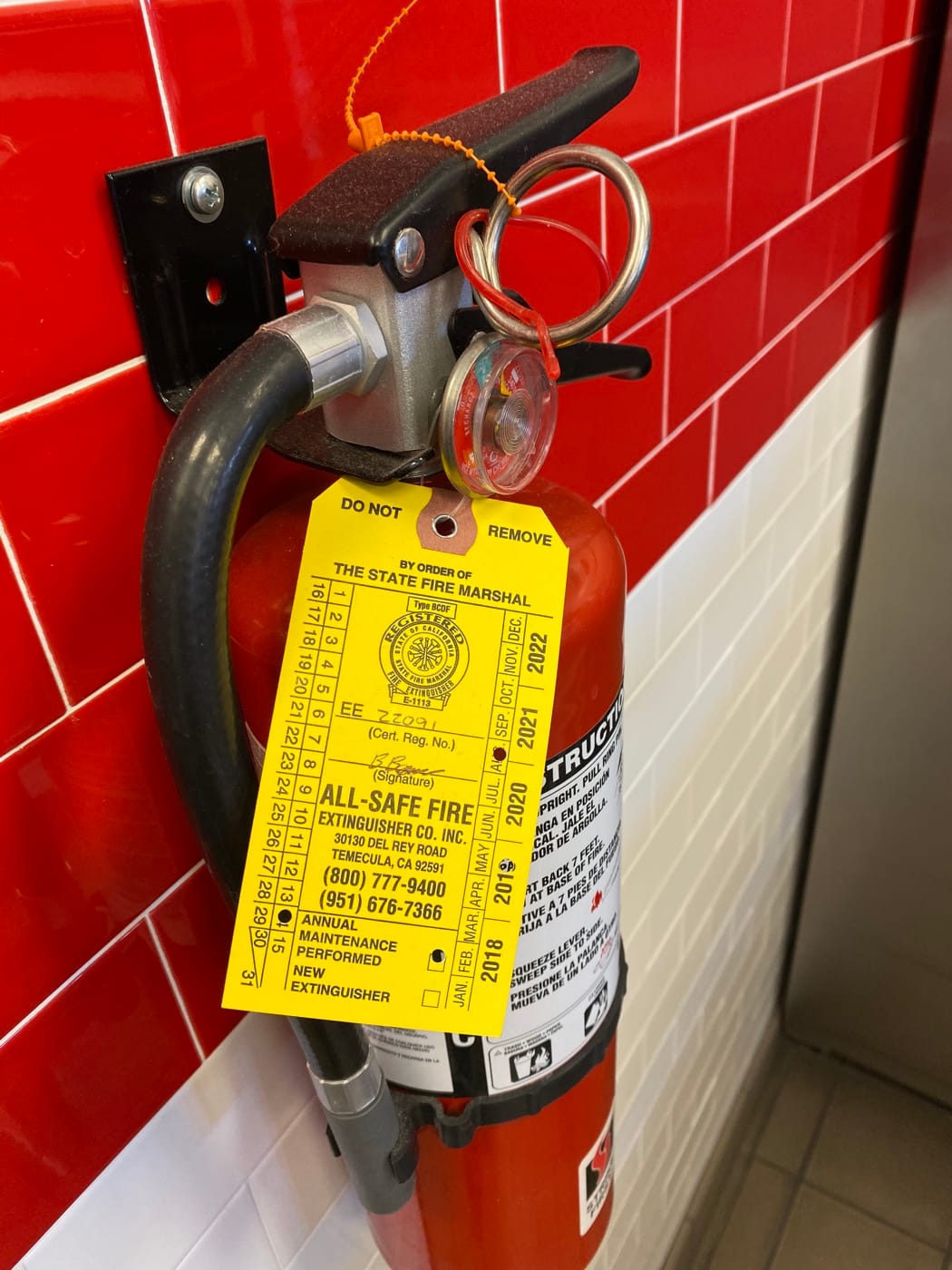 Wall-mounted portable extinguisher with a yellow All-Safe service tag